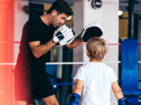 Male boxing mentor spars with young boy in boxing ring