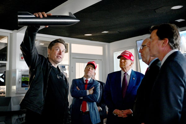 Elon Musk holds up a miniature model of SpaceX's Starship as Donald Trump and other visitors look on