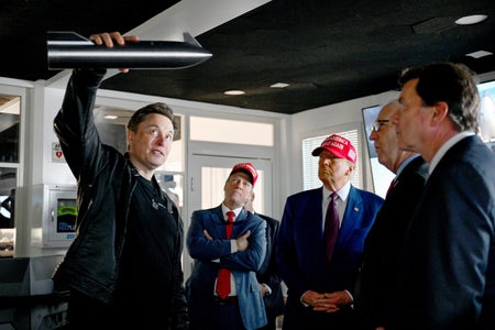 Elon Musk holds up a miniature model of SpaceX's Starship as Donald Trump and other visitors look on