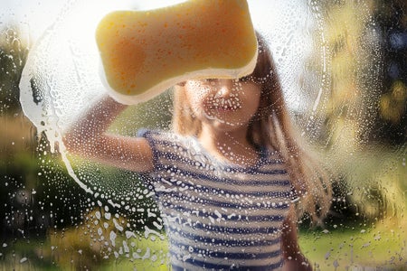Girl washing window with sponge and soapy water, outside on a sunny day