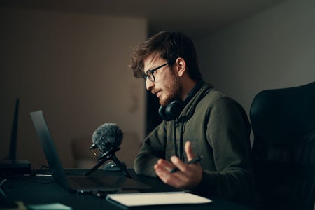 Side view of a young bearded person speaking into a microphone at a laptop