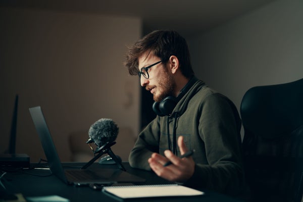 Side view of a young bearded person speaking into a microphone at a laptop