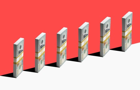 6 bundles of US $100 bills standing vertically on edge of white shelf.