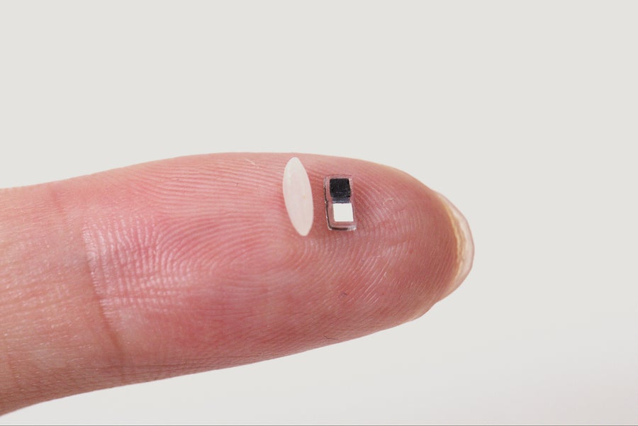 A tiny pacemaker sits next to a single grain of rice on a fingertip