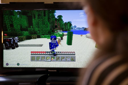 View from behind of a person sitting in front of a screen, playing Minecraft on a video game console