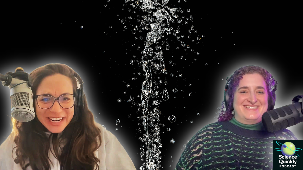 Two women sit with microphones laughing and a water spray in the background separates them